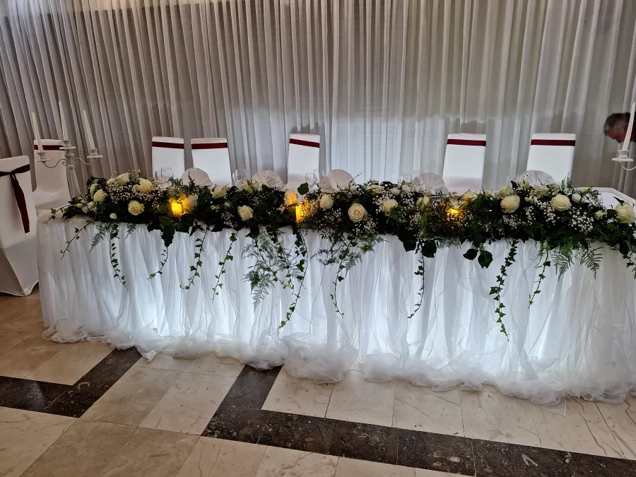 Dekoriran stol za mladence u sali za vjenčanje sa svježim cvijećem i bijelim ružama.