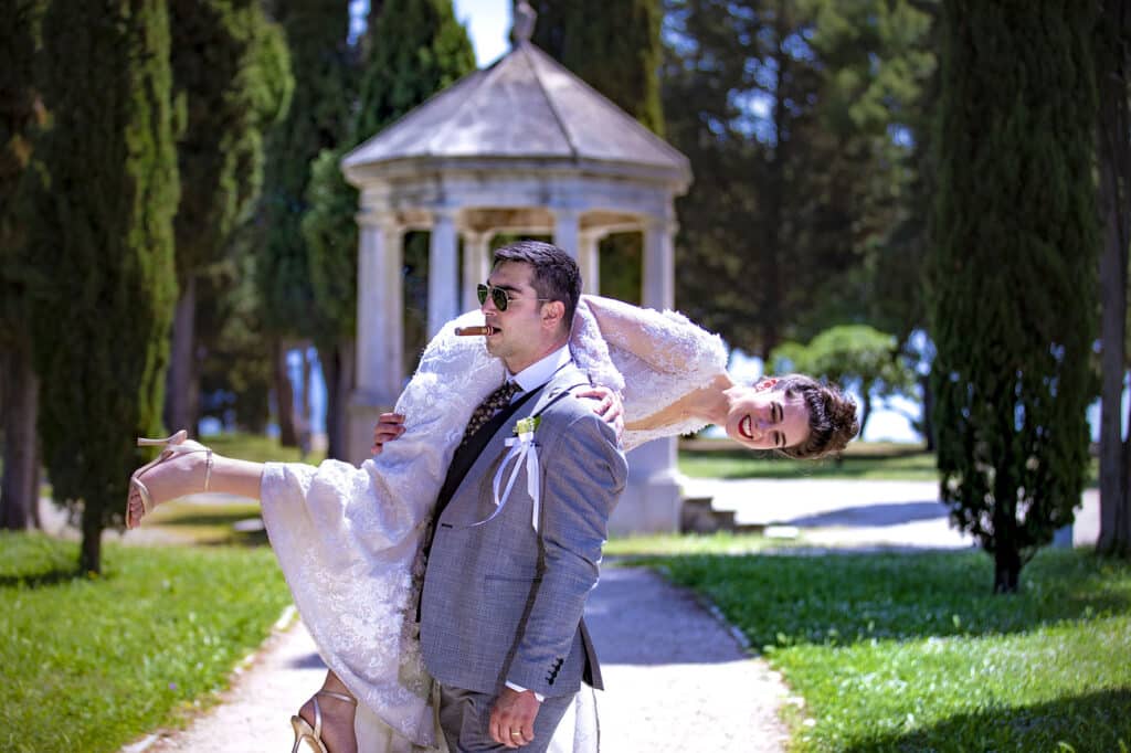 Mladoženja nosi mladu u bijeloj vjenčanici preko ramena.