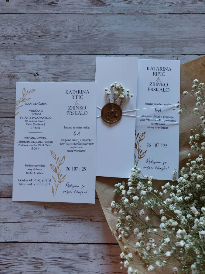 Pozivnica za vjenčanje na bijelom papiru s zlatnim grančicama masline i zlatnim pečatom.