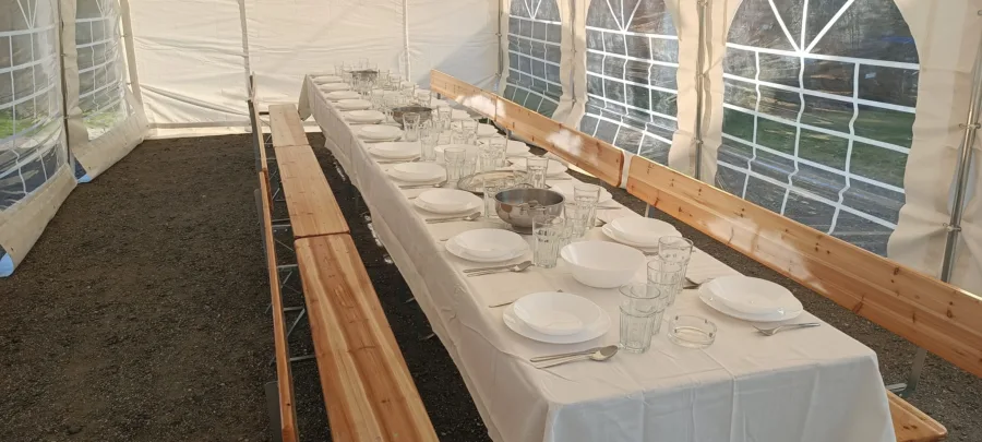 Posložen stol s drvenim klupama u šatoru za vjenčanje.