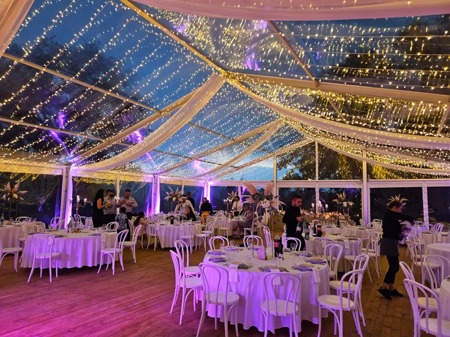 Elegantan šator za vjenčanje s okruglim bijelim stolovima i lampicama.