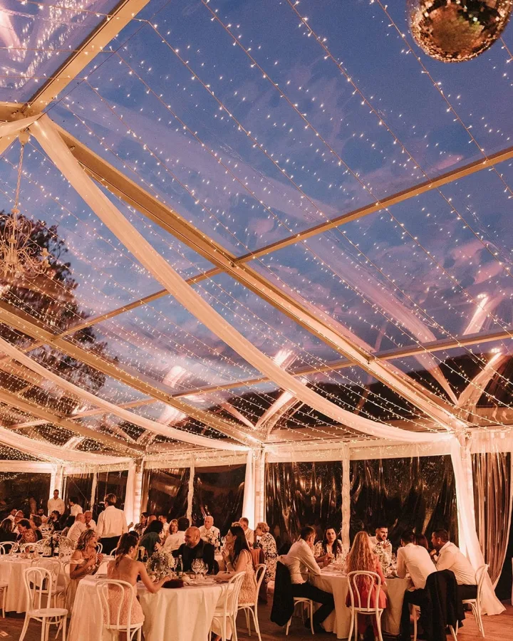 Gosti na vjenčanju sjede pod lampicama šatora.