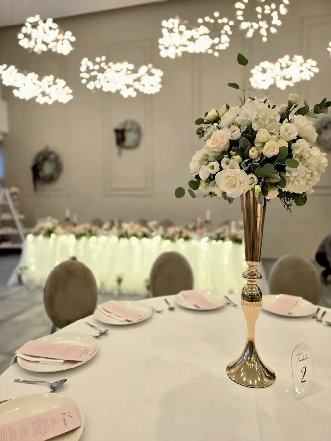 Zlatna vaza s bijelim ružama kao centralni dio dekoracije stola za goste u sali za vjenčanje.