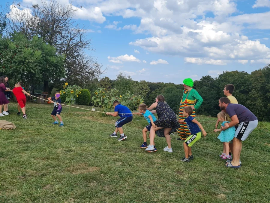 Djeca navlače konop igrajući igru "povlačenja konopa" za vrijeme proslave, dok ih klaun zabavlja i nadgleda.