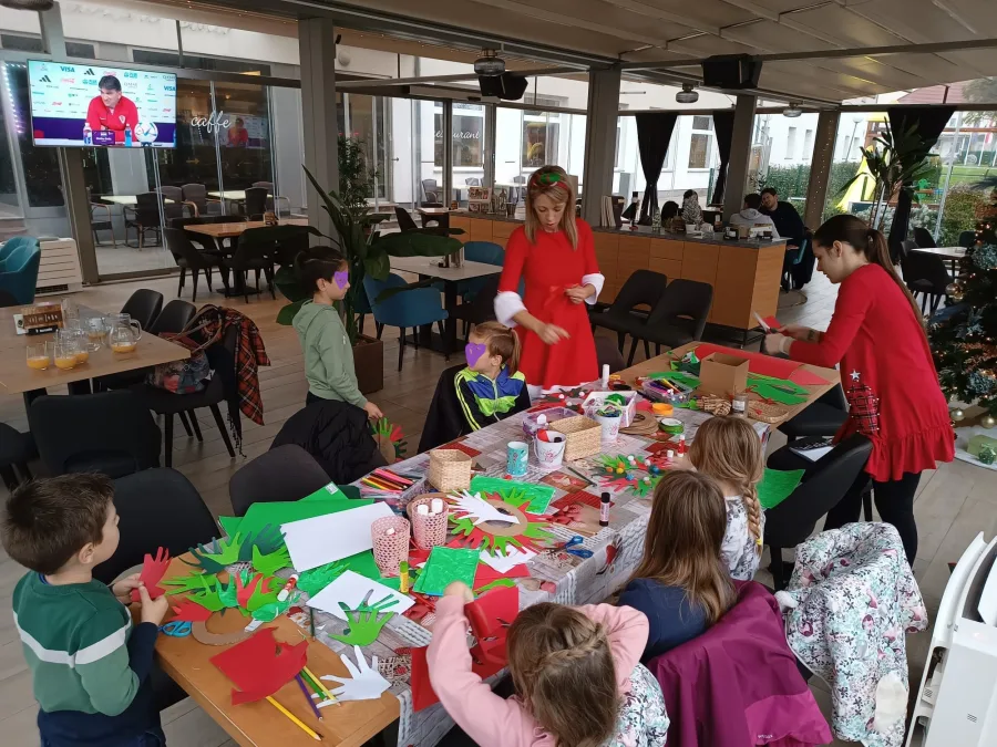 Djeca za stolom igraju igre rezući kolaž papir dok ih animatori nadgledaju za vrijeme Božića.