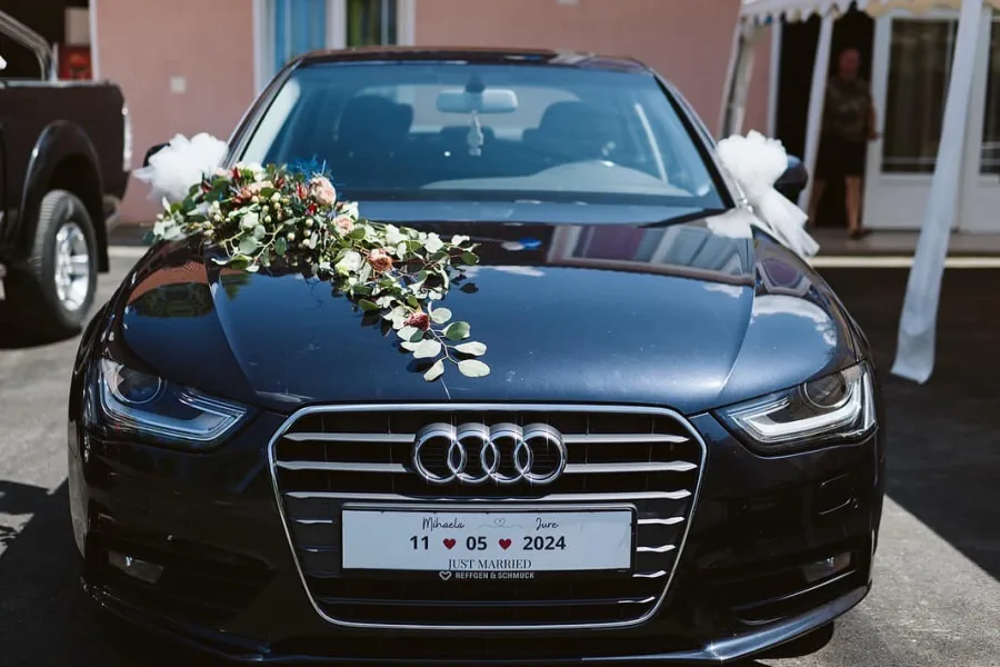 Auto za mladence marke Audi ukrašen cvijećem i na mjestu tablica piše datum vjenčanja i imena mladenaca.