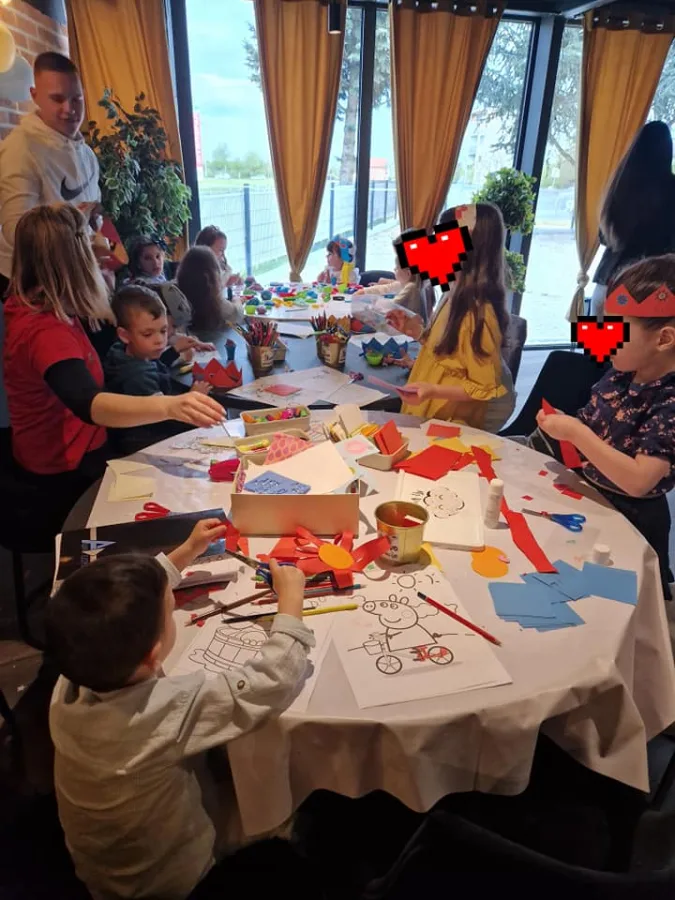 Djeca bojaju za stolom dok ih animatori čuvaju.