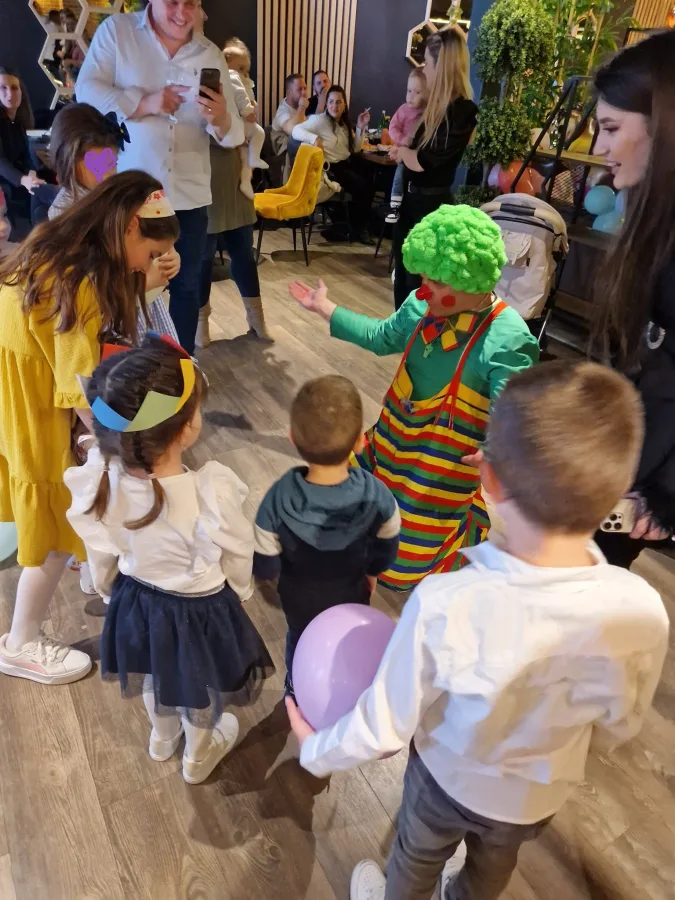 Klaun zabavlja djecu urestoranu tijekom proslave, a roditelj ih fotografira mobitelom.