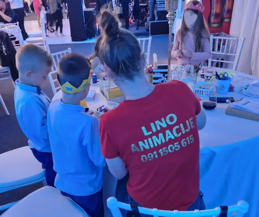 Animatorica na vjenčanju se igra s djecom za stolom.