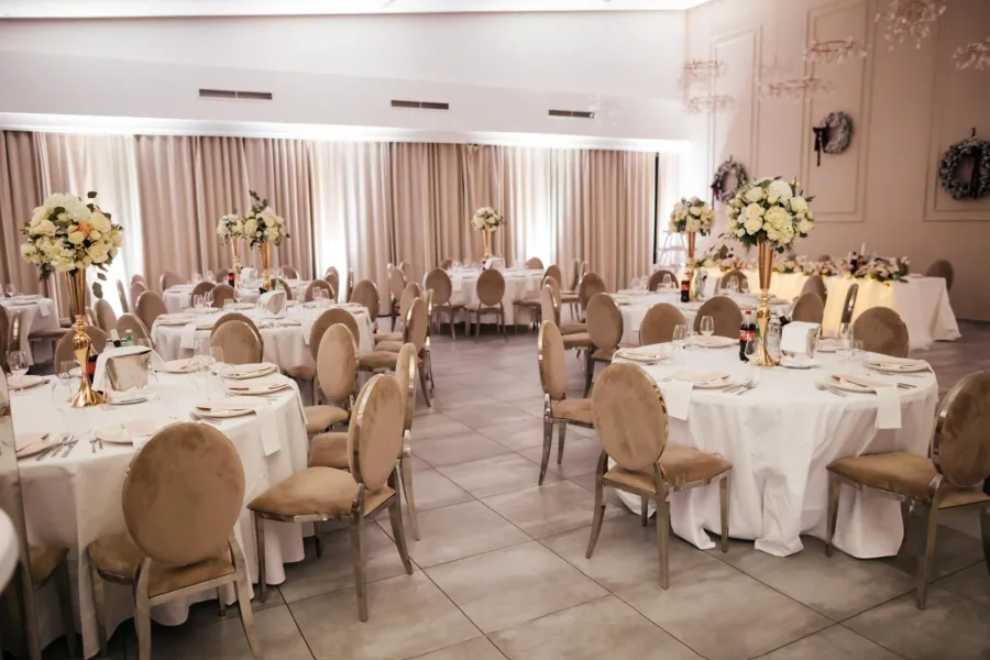 Dekorirana sala za vjenčanje sa smeđim stolicama, bijelim stolnjacima te zlatnim vazama u kojima su bijeli buketi cvijeća.