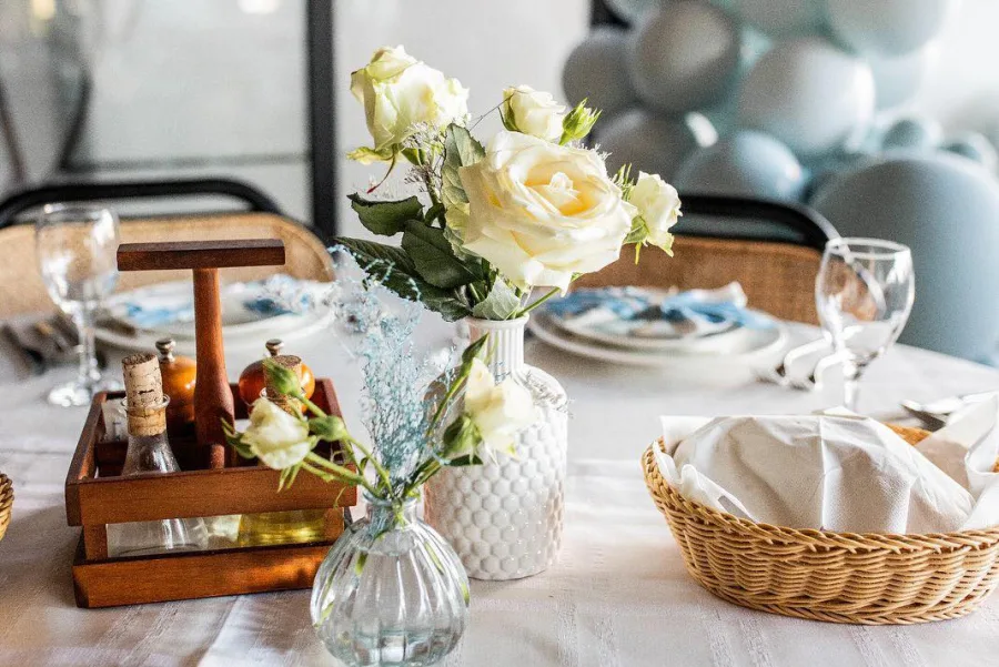 Bijelo i plavo cvijeće u vazama kao centralna dekoracija stola za uzvanike na vjenčanju u sali.