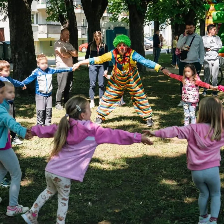 Djeca se drže za ruke u krugu s klaunom igrajući se.
