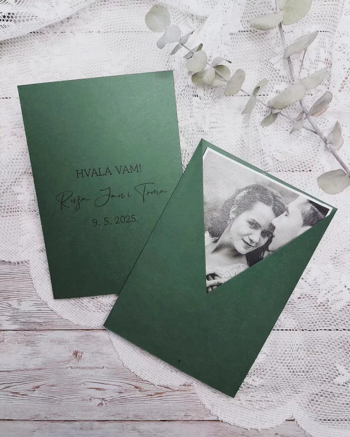 Crno bijela fotografija mladenaca u zelenoj poluotvorenoj kuverti kao zahvalnica za vjenčanja. Na poleđini se nalaze njihova imena i datum vjenčanja.