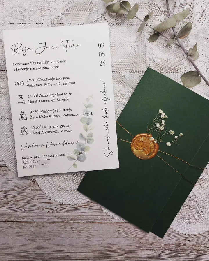 Pozivnica za vjenčanje na bijelom papiru i zeena kuverta s zlatnim pečatom i malim bijelim cvijećem.