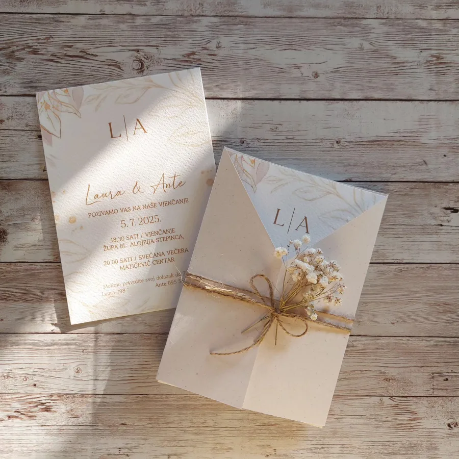 Pozivnica u krem boji s akvarel cvijećem u poluotvorenoj krem kuverti omotana mašnom od jute i bijelim cvijećem.