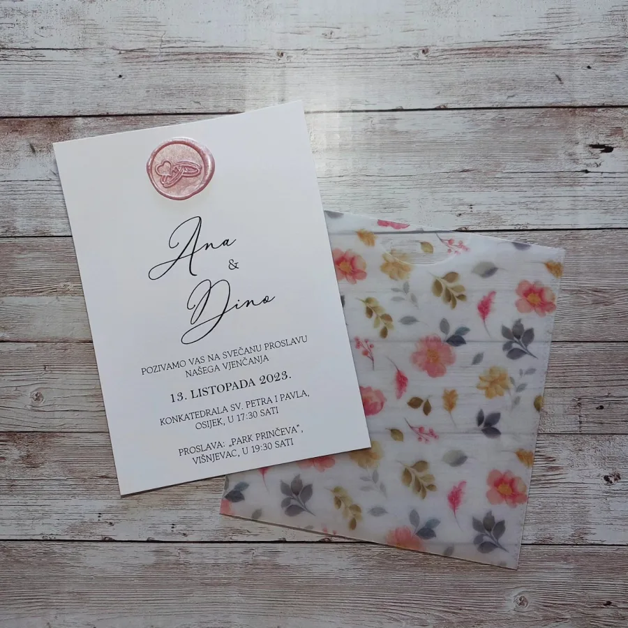 Pozivnica za vjenčanje na bijelom papiru, ružičastim pečatom i prozirnkastim omotom s šarenim cvijećem.