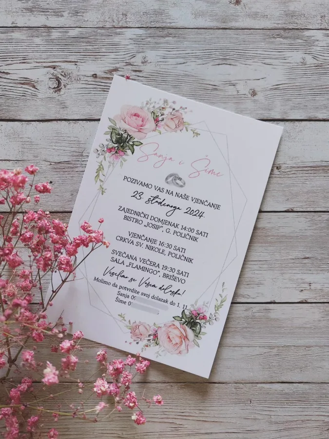 Pozivnica za vjenčanje s ružičastim ružama, imenima mladenaca i srebrenim prstenom ispod imena.