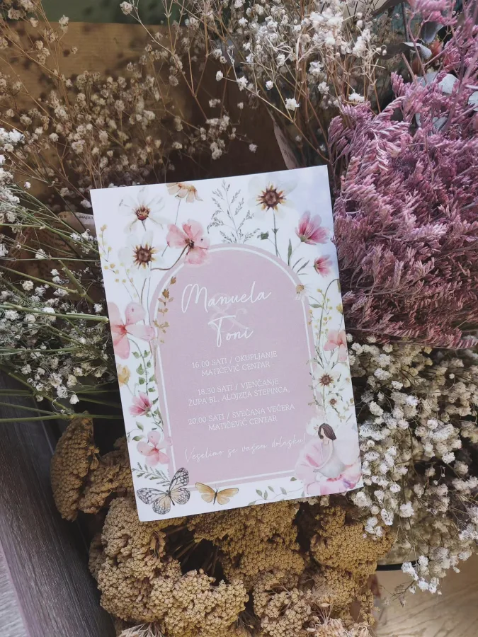 Pozivnica za vjenčanje na bijelom papiru u sredini rozi dio s imenima mladenaca ukrašena s ružičastim cvijećem i leptirima.