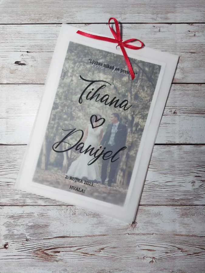 Zahvalnice za goste na vjenčanju s fotografijom mladenaca, datumom vjenčanja i imenima. Crvena mašnica je a vrhu, a preko fotografije je zamagljen papir.