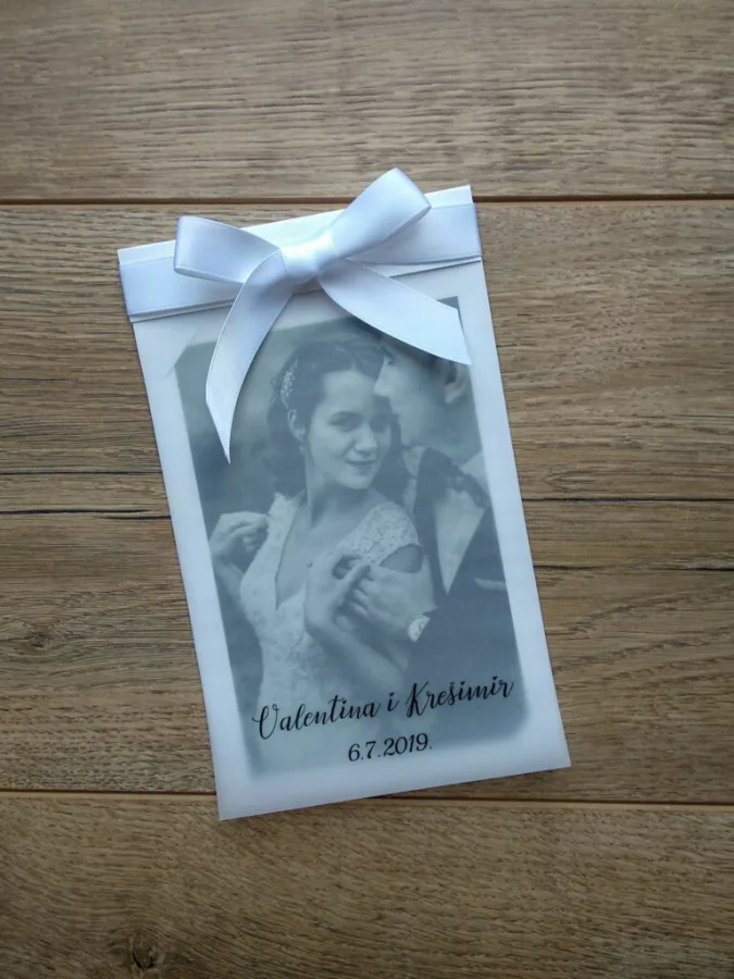 Zahvalnica za vjenčanje s fotografijom mladenaca. Preko fotografije je zamagljen papir s njihovim imenima i datumom vjenčanja i baby plavom mašnicom na vrhu.