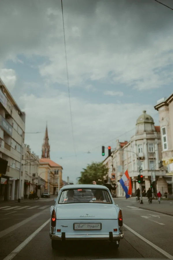 Mladenci u svijetloplavom oldtimer Peugeotu voze se kroz grad.