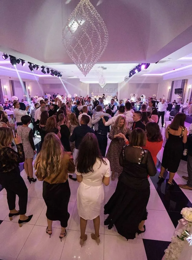 Uzvanici plešu na podiju u sali za vjenčanje.