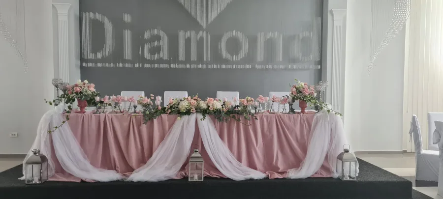 Stol mladenaca s ružičastim stolnjakom i bijelim i ružičastim cvijećem u sali za vjenčanje.