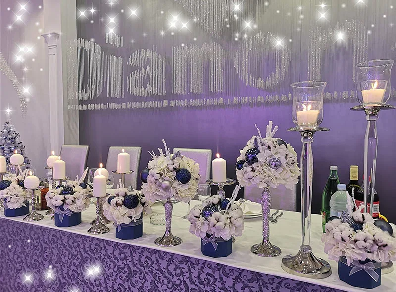 Stol mladenaca u sali za vjenčanje ukrašen aranžmanima bijelog cvijeća s plavim kuglicama.