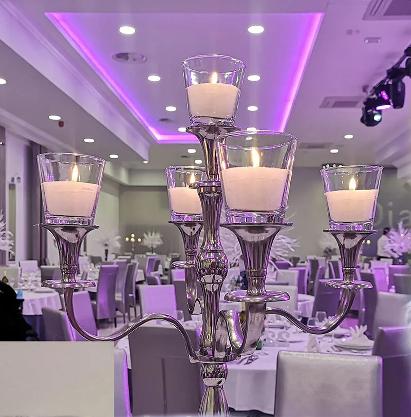 Srebreni svijećnjak s upaljenim svijećama u sali za vjenčanje kao središnja dekoracija na stolu.