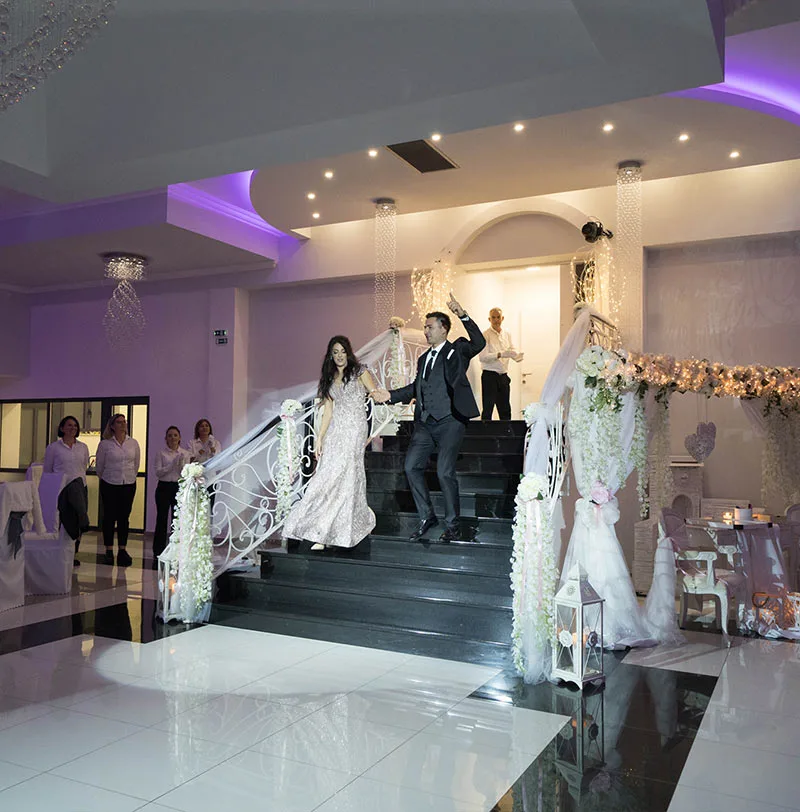 Mladenci silaze stepenicama na podij u sali za vjenčanje.