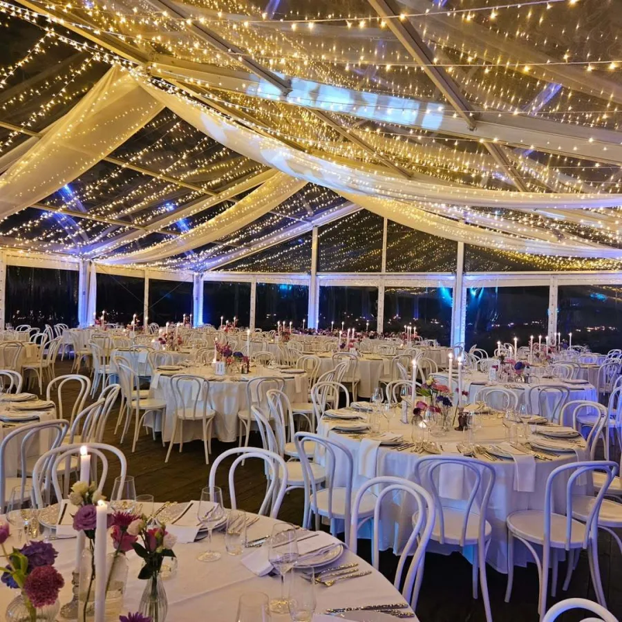 Dekoriran šator za vjenčanje s bijelim okruglim stolovima i lampicama Heritage Event Venue.