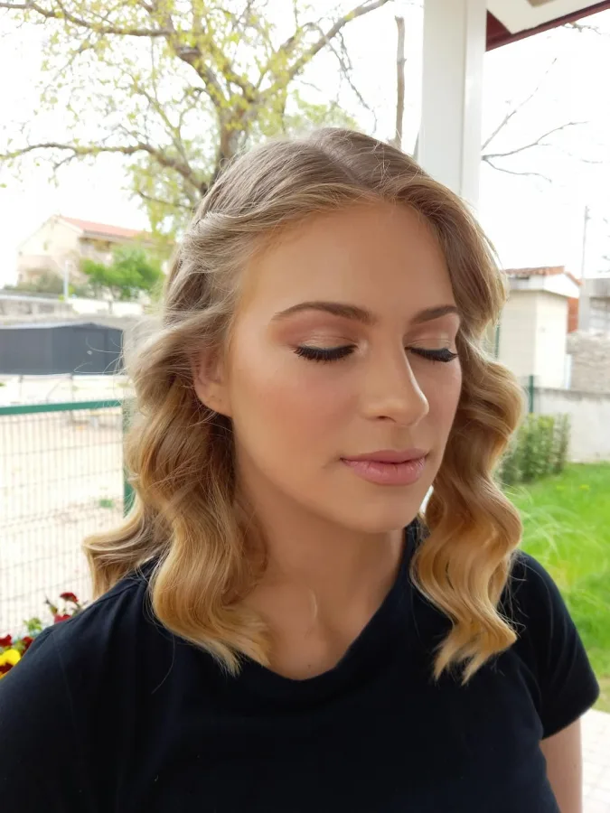 Žena valovite plave kose svečano našminkana.