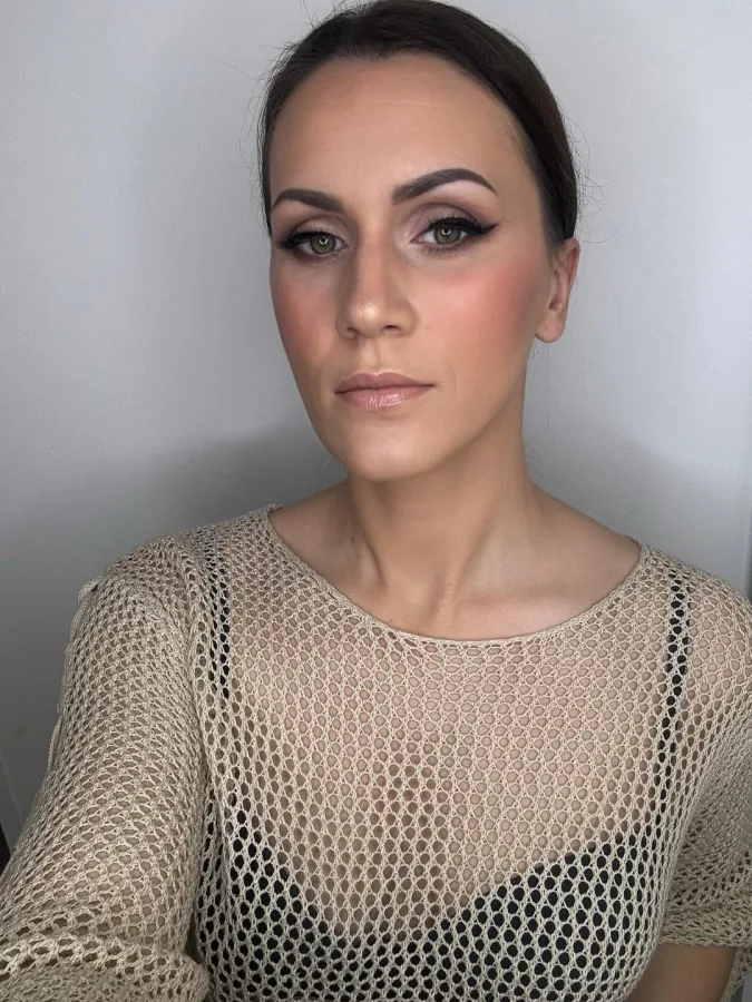 Starija žena crne kose u repu našminkana s istaknutim očima.