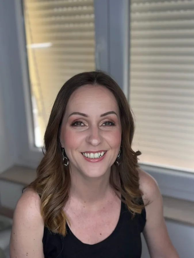 Starija žena valovite smeđe kose, nasmijana i našminkana s rumenilom.