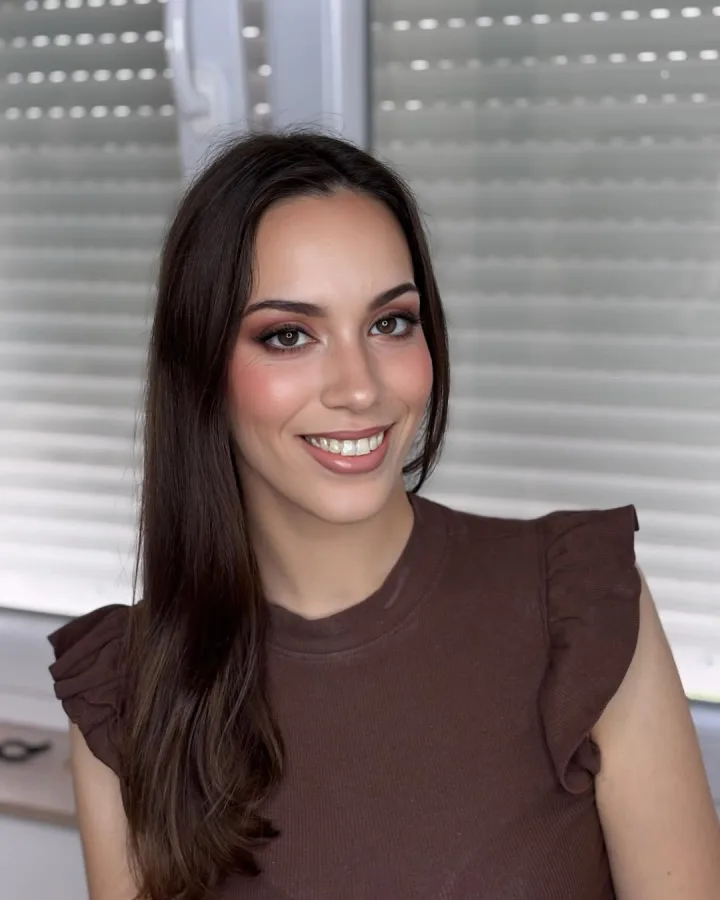 Cura duge smeđe kose nasmijana i našminkana s istaknutim očima.