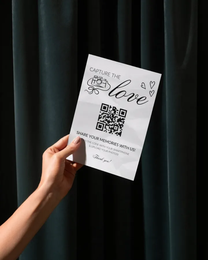 Ruka koja drži papir s QR kodom kojeg gosti vjenčanja mogu skenirati kako bi prenijeli svoje fotografije.