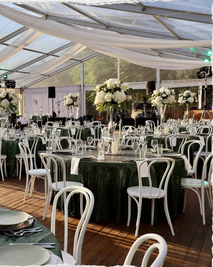 Zeleni stolovi dekorirani bijelim cvijećem za vjenčanje pod šatorom u prirodi.