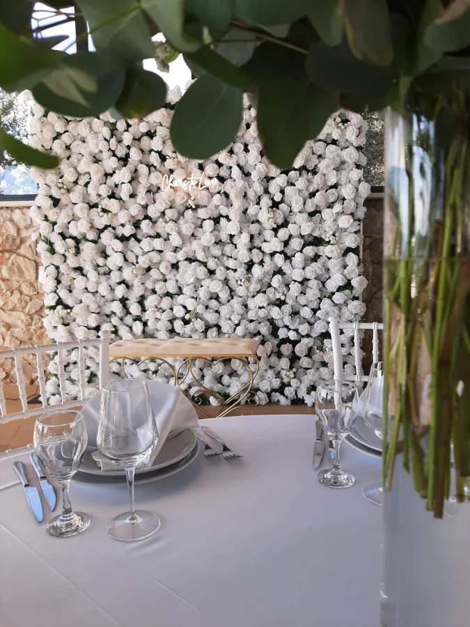 Bijeli okrugli stol za vjenčanje i cvijetni zid od bijelih ruža s neonskim natpisom "Cheers to love".