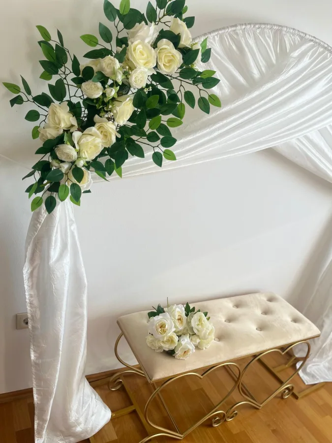 Girlanda s satensko bijelim platnom , buketom ruž a i zlatna sjedalica kao kutak za slikanje.
