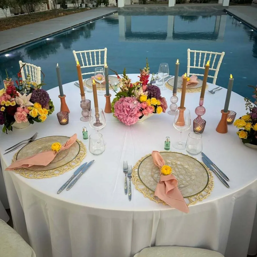 Okrugli stol za vjenčanje s šarenim cvijećem, svijećama i salvetama uz bazen.