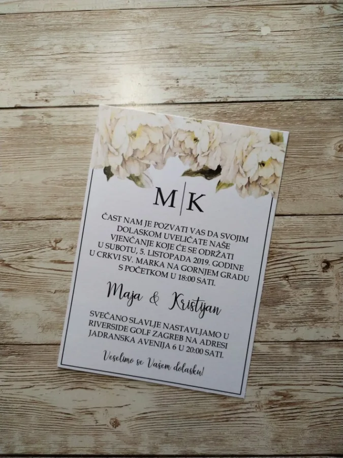Pozivnica za vjenčanje na bijelom papiru s bijelim cvijećem na vrhu.