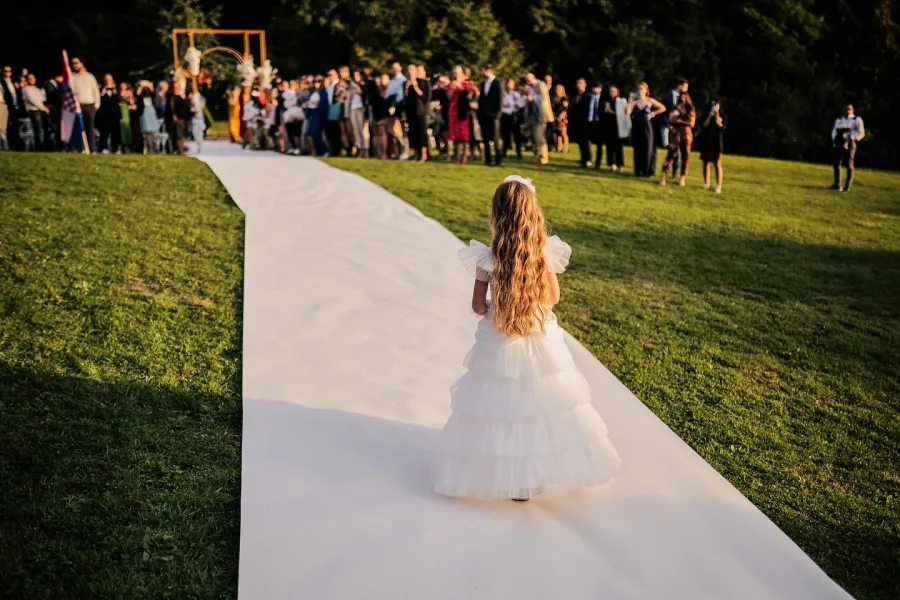Mala djeveruša hoda bjelim tepihom na vjenčanju u prirodi u Zagrebu.