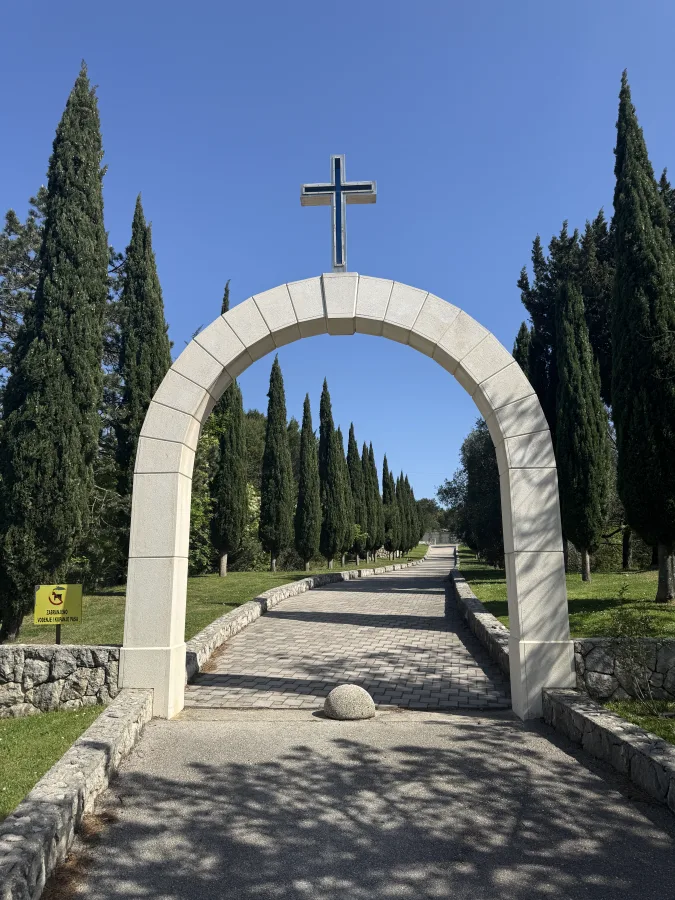 Svod od bijelog kamena s križem na vrhu pri ulazu u dvorište crkve.