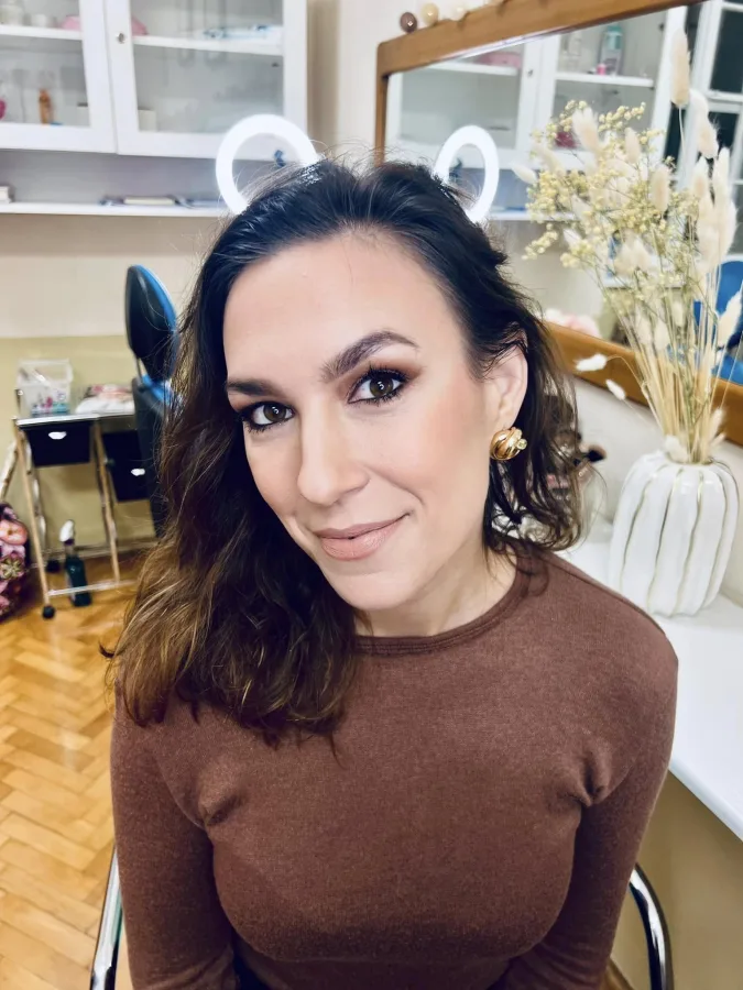 Djevojka našminkana sa smeđim sjenilom, crnom olovkom za oči, umjetnim trepavicama i nude ružom.