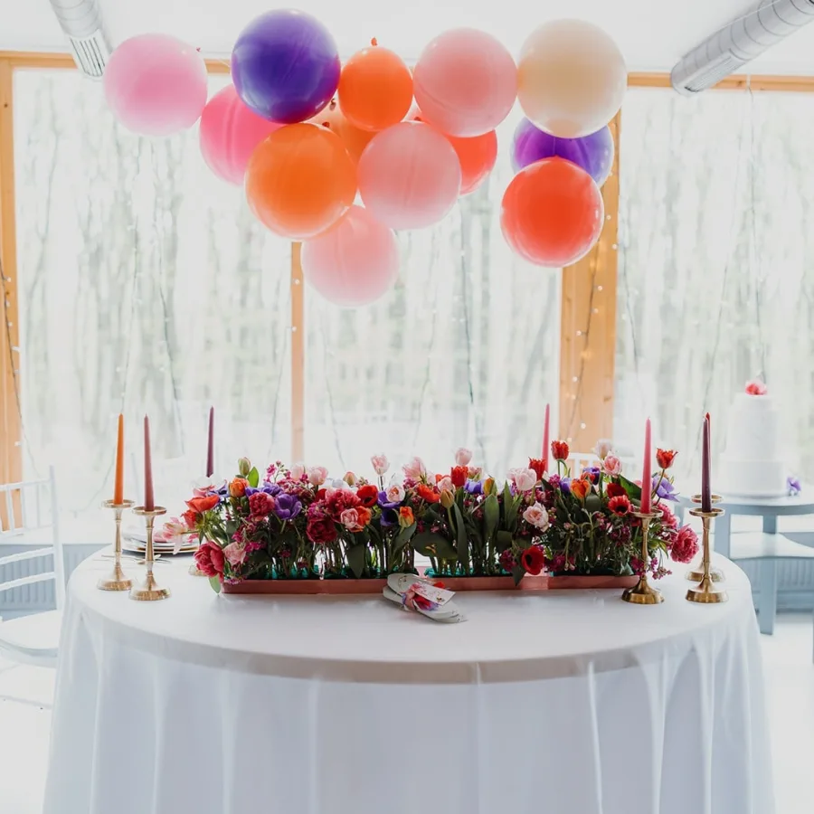 Bijeli stol s cvijećem i svijećama iznad kojeg su baloni.