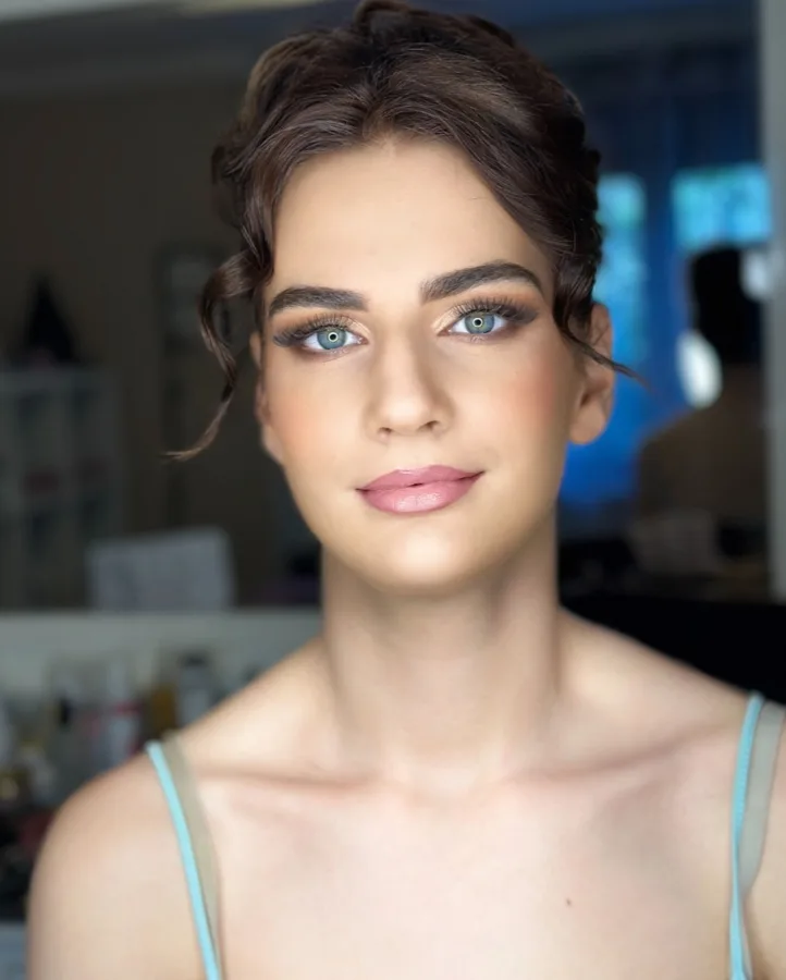 Djevojka plavih očiju našminakana s ružičastim ružom i lagano naglašenim očima.