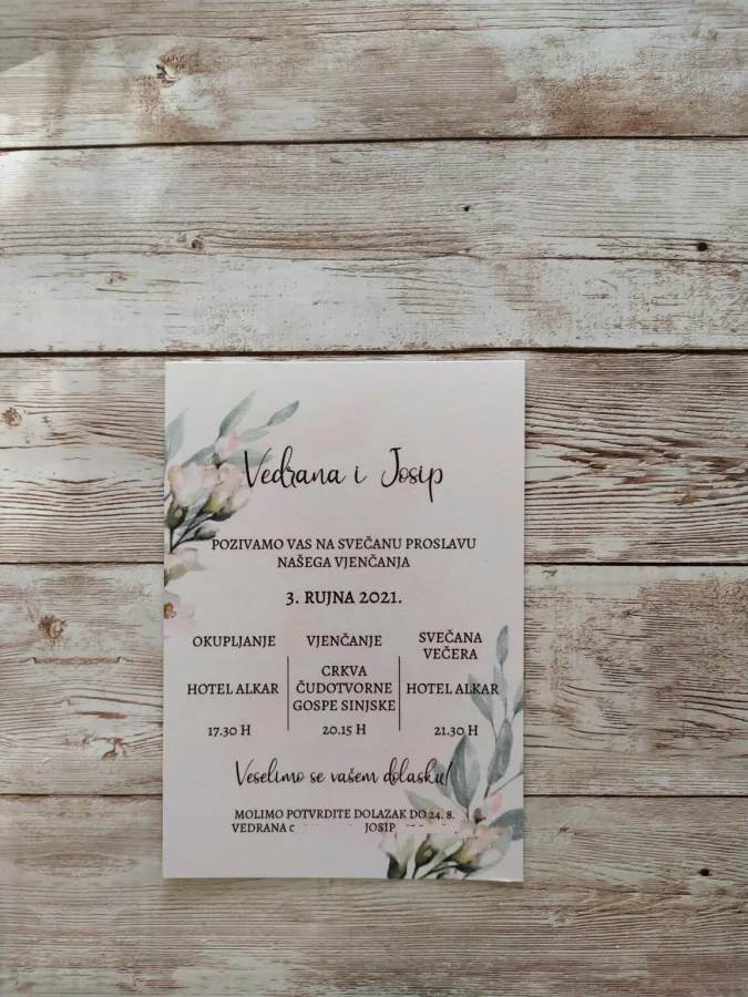 Pozivnica za vjenčanje na bijelom papiru s bijelkastim cvijećem i granama masline.