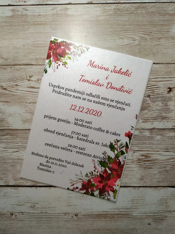 Pozivnica za vjenčanje na bijelom papiru ukrašena crvenom božićnom zvijezdom.