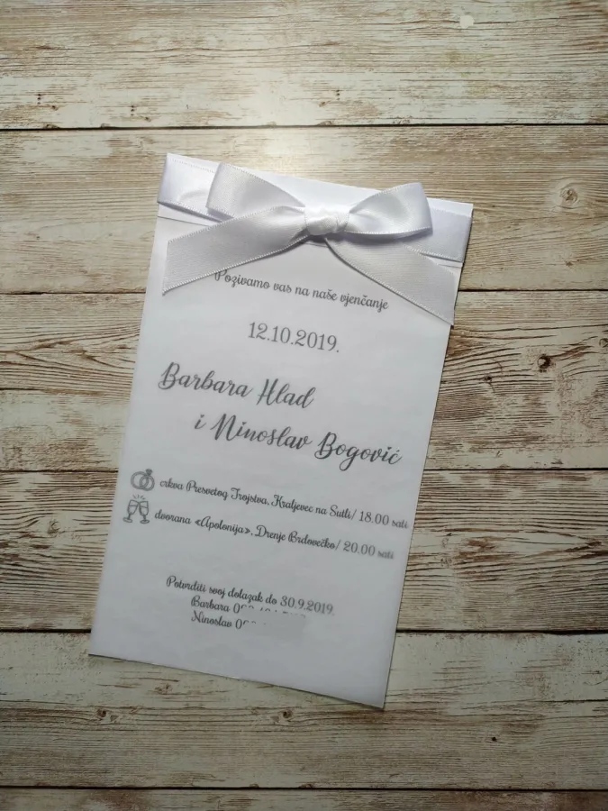 Pozivnica za vjenčanje na bijelom papiru s srebrenom mašnom na vrhu.