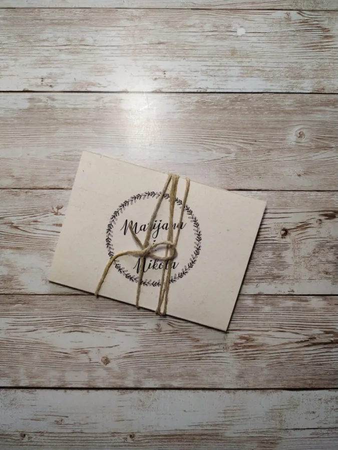 Pozivnica za vjenčanje s konopčićem mašnom, imenima mladenaca na bijelkastom papiru.